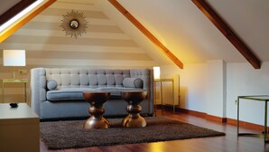 A loft-style room with a sloped ceiling, a tufted sofa, two side tables, and a decorative wall piece.