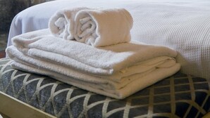 A neatly made bed with folded towels, a lamp on a bedside table, and a stone wall in the background.