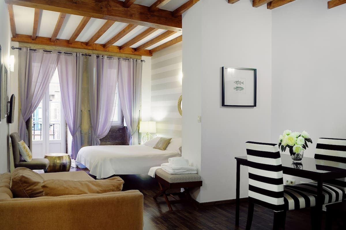 A hotel room with a bed, a sofa, a dining table with chairs, and a window with curtains.