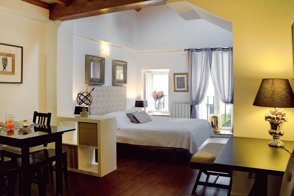 A bedroom with a bed, bedside table, lamp, and a window with curtains.
