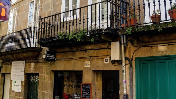 A stone building with multiple windows, a green door, and a balcony with plants.