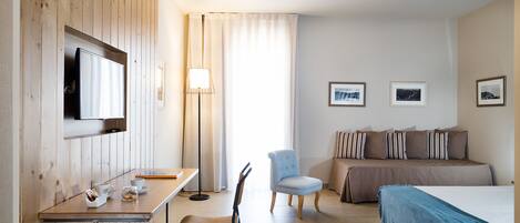 Une chambre d’hôtel avec un mur lambrissé en bois, un téléviseur à écran plat, un bureau avec une chaise, un lit recouvert d’une couverture bleue et une petite table ronde avec une tasse et une soucoupe.