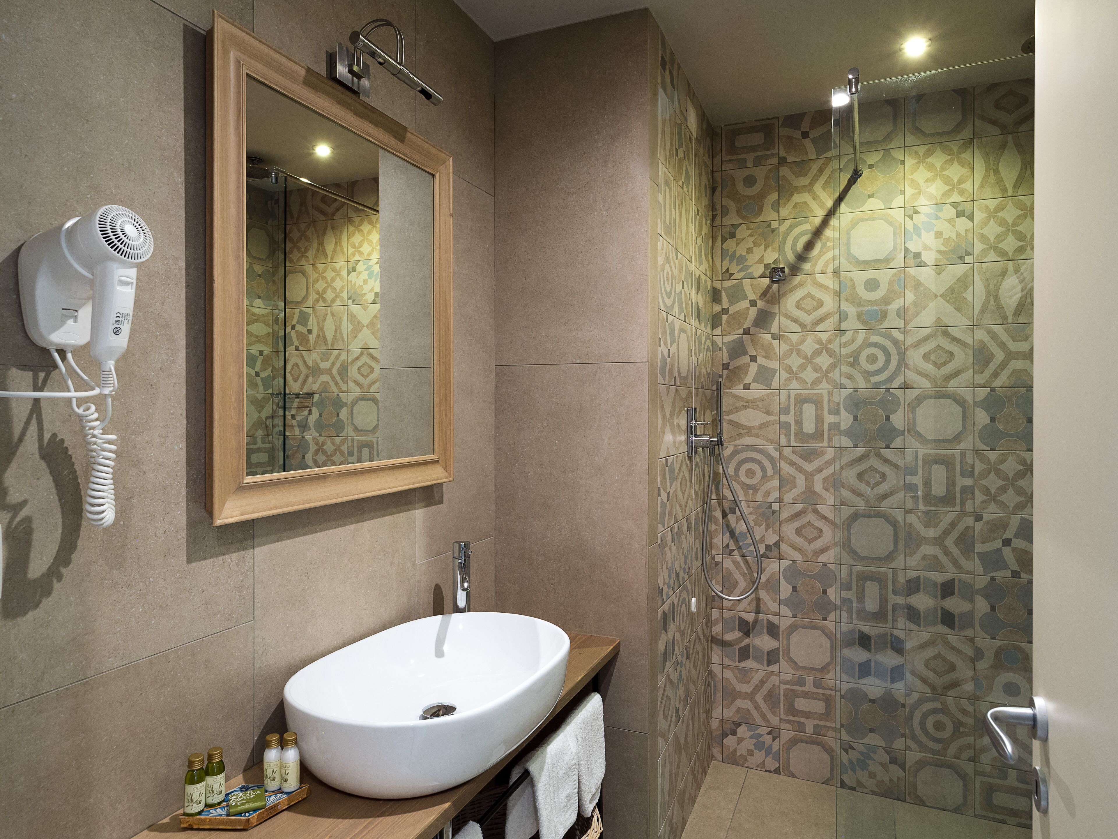 Een badkamer met een grote spiegel, een wastafel, een haardroger en een douche met betegelde muren.
