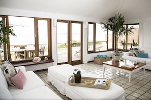 A bright living room with a white sofa, a wooden coffee table, and a large window overlooking a patio with outdoor furniture. - Villa da Praia Buzios (Búzios)