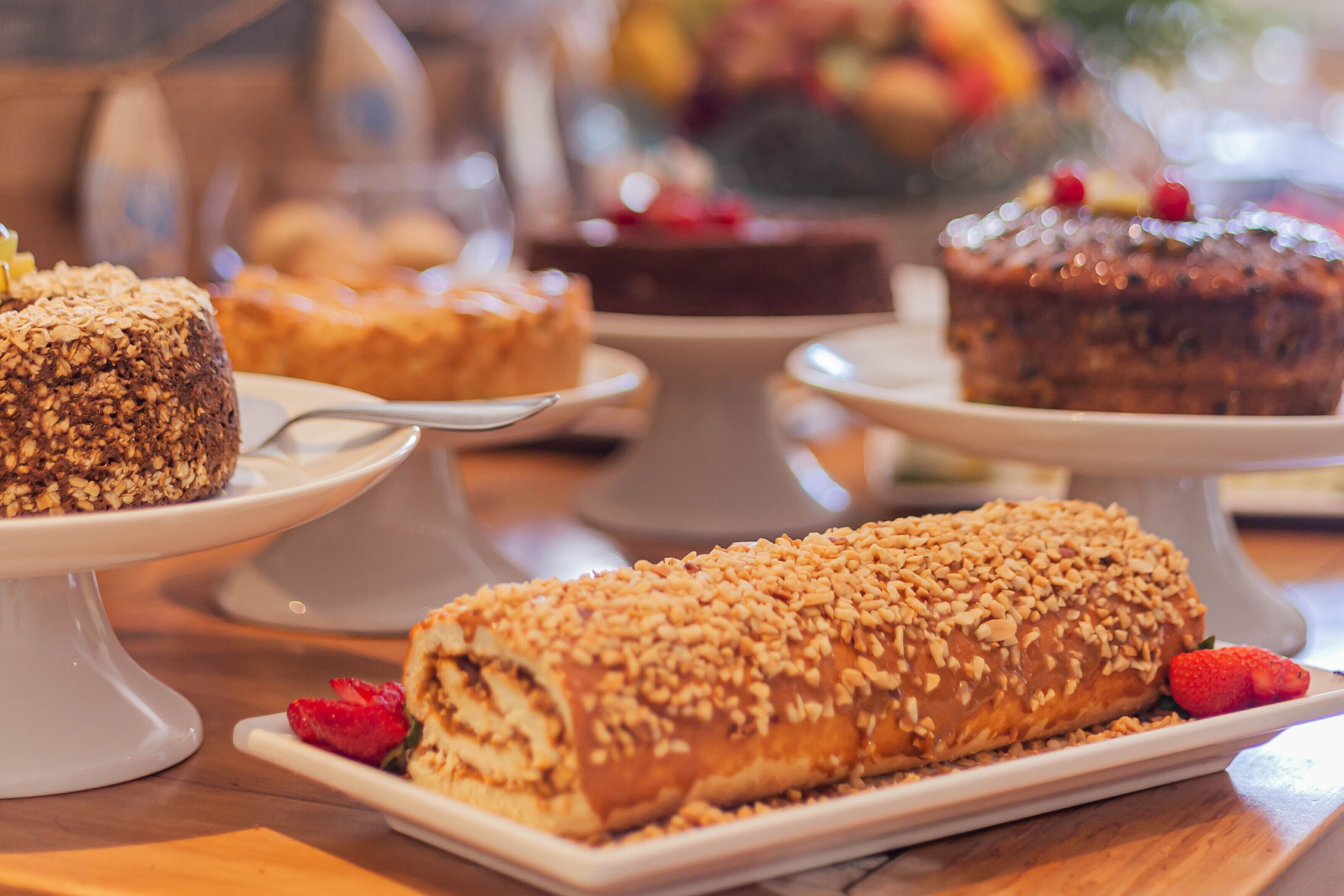 A variety of desserts on white cake stands, including a rolled pastry with nuts and a chocolate cake with berries.