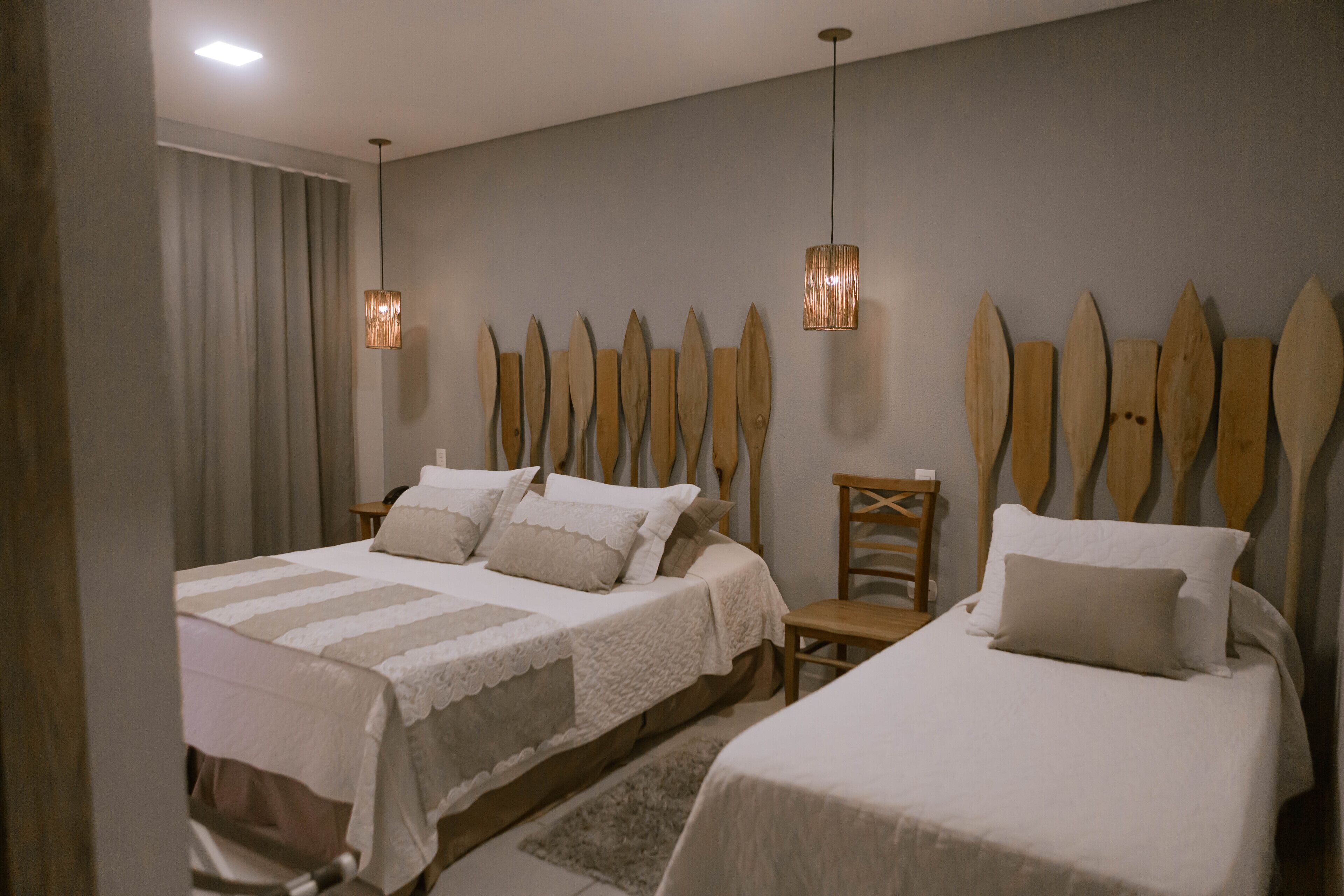 A bedroom with two beds, a wooden headboard, a small table, and a hanging light fixture.
