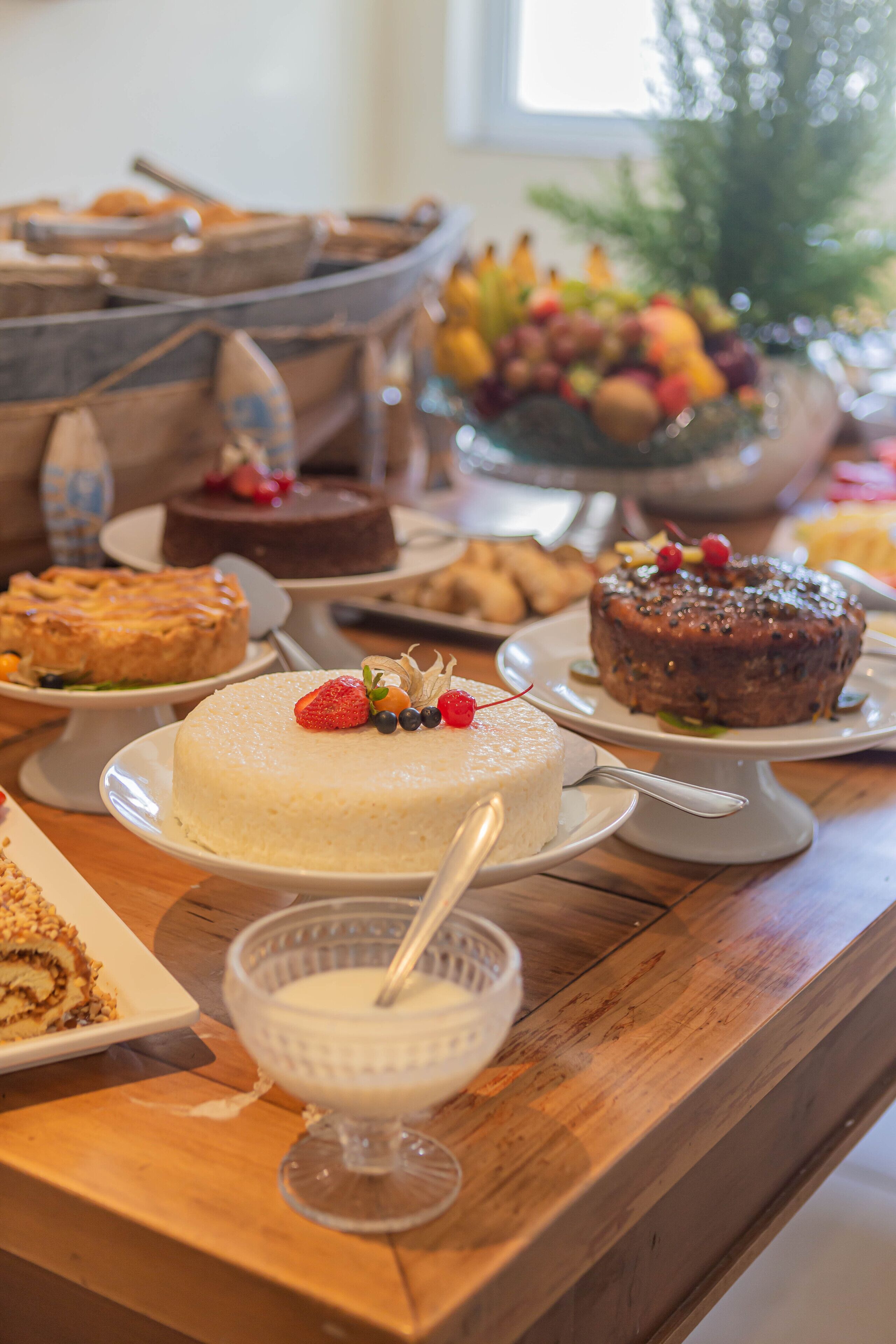 A wooden table with various desserts, including cakes and a bowl of fruit.