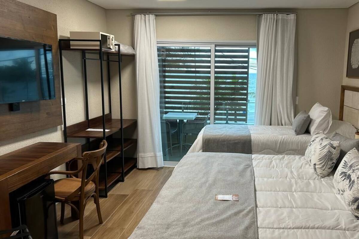 A hotel room with a bed, a desk, a chair, a TV, and a balcony with curtains.