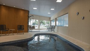 An indoor swimming pool with a tiled edge, surrounded by seating areas and large windows. - Hotel VillaReal Charme (Guaratuba)