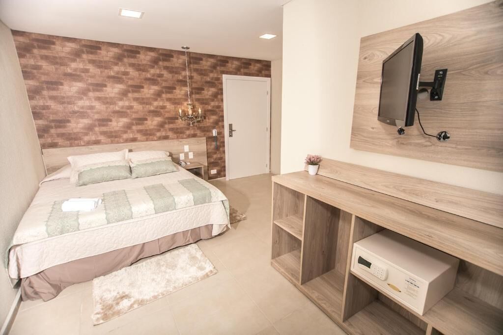 Un dormitorio con cama, mesitas de noche, televisor montado en la pared y una consola de madera con cajón.