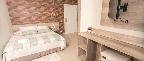 Un dormitorio con cama, mesitas de noche, televisor montado en la pared y una consola de madera con cajón.