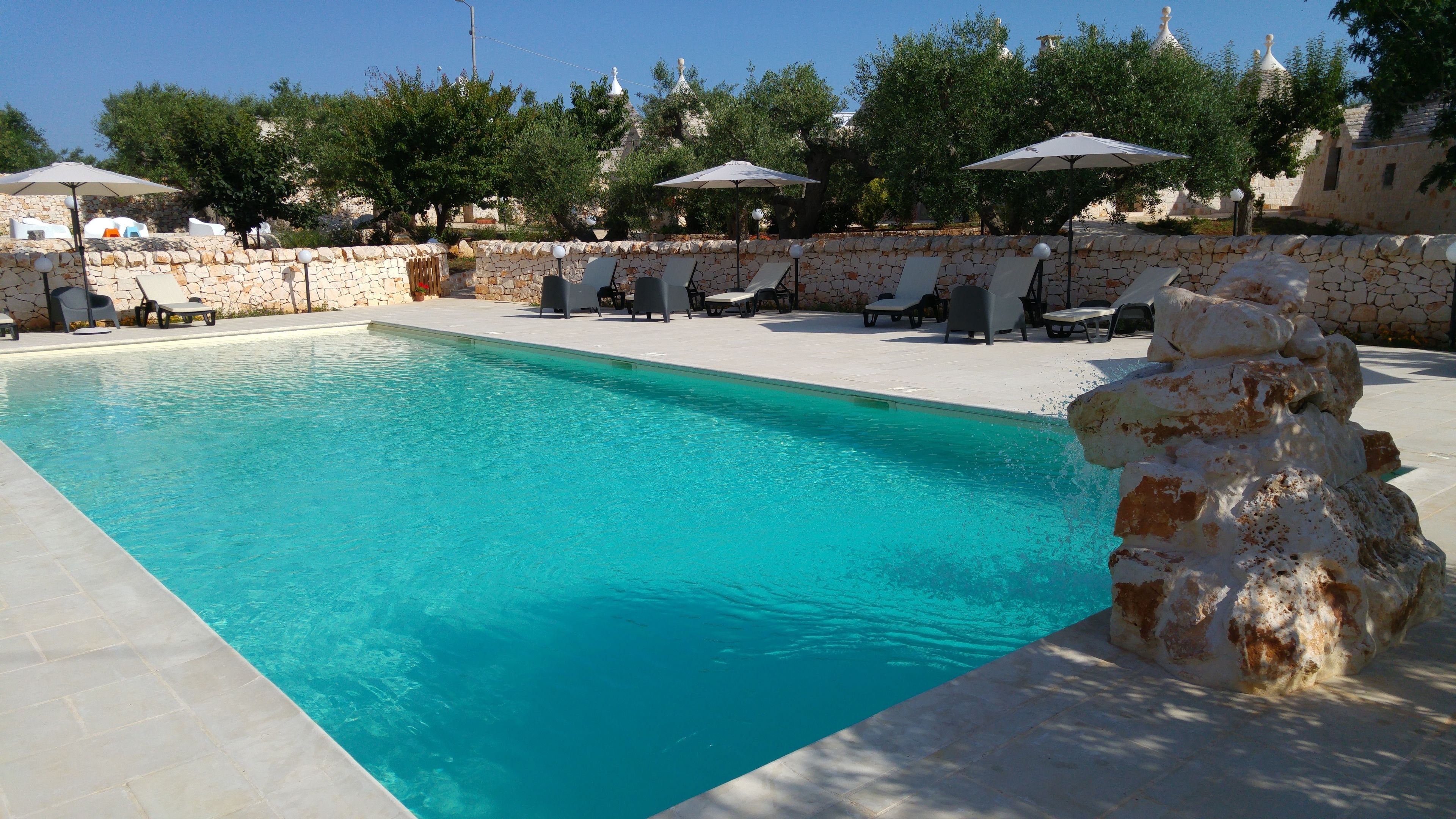 A clear blue pool with stone walls and lounge chairs.