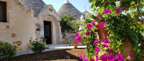 A rustic stone building with multiple domed roofs, a small entrance, and a garden with flowering plants.