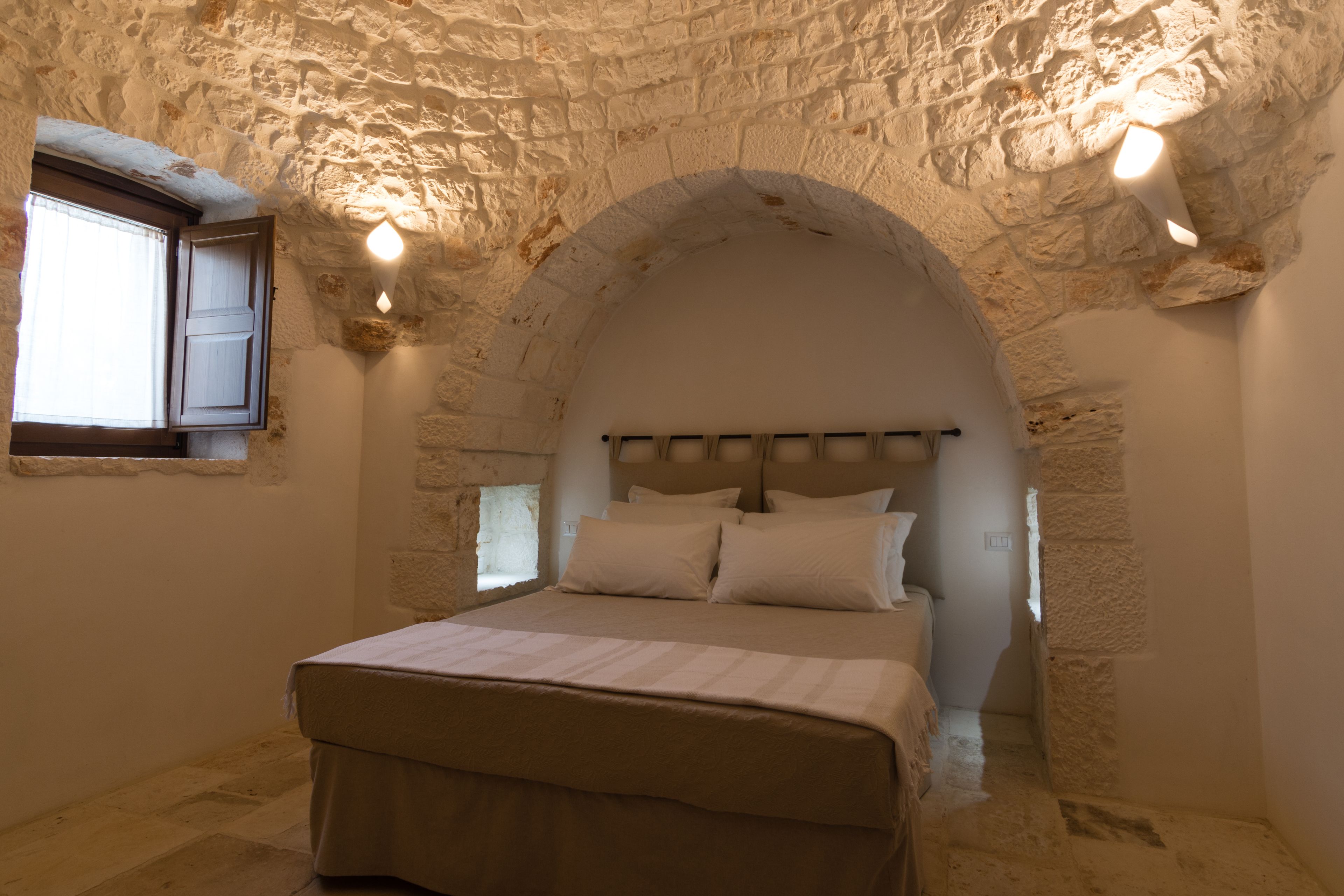 Una camera da letto con un arco in pietra, un letto con lenzuola bianche e due luci a parete.