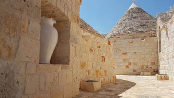 A stone corridor with a white vase in a niche, leading to a building with a conical roof.