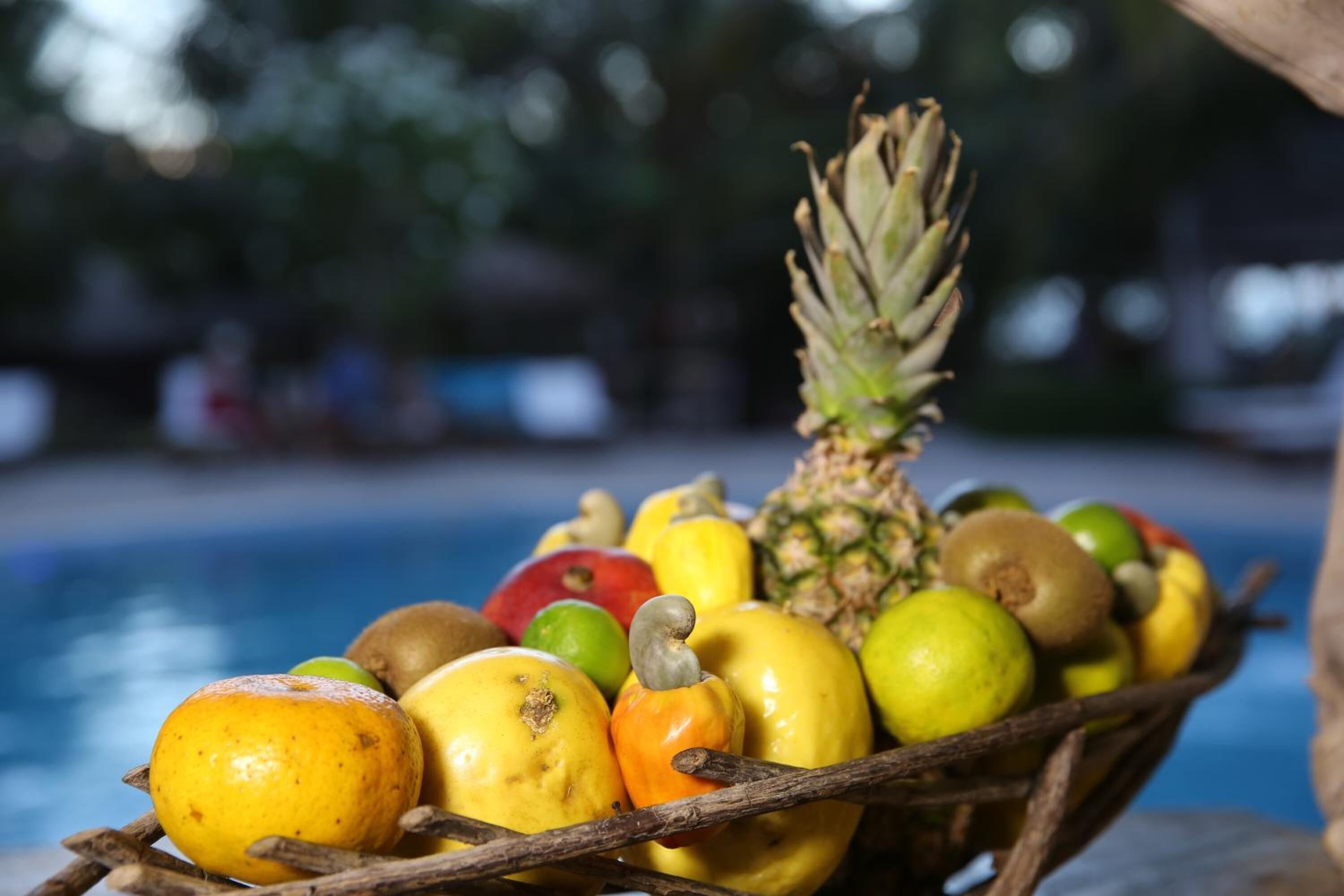 A wooden basket filled with various fruits including apples, bananas, and a pineapple, placed near a pool.