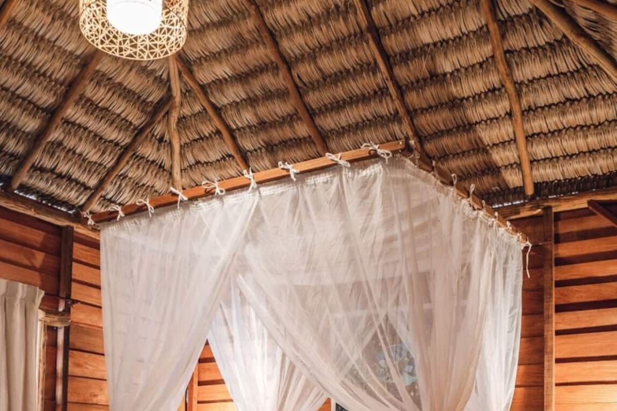 A room with a thatched roof, wooden walls, a bed with a canopy, and a hanging light fixture.