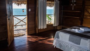 Una habitación de madera con una cama, vista a la playa y una hamaca afuera.