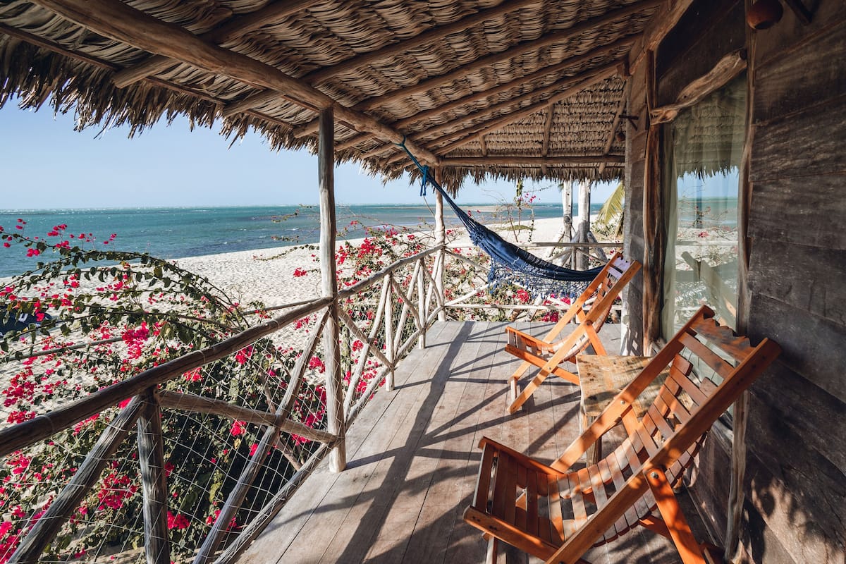 A wooden deck with a thatched roof overlooking a beach.