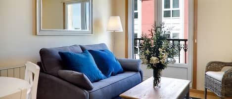 A modern living room with a grey sofa, blue cushions, a wooden coffee table, and a vase with flowers.