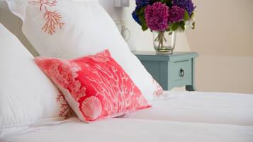 Un letto con cuscini bianchi e rossi, un vaso con fiori e un comodino azzurro.