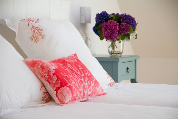 A bed with white and red pillows, a vase with flowers, and a light blue nightstand. - Apartamentos Duerming Sea View Viveiro (Viveiro)