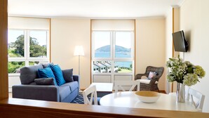 A room with a grey sofa, a dining table with a bowl, a wicker chair, and a TV mounted on the wall. - Apartamentos Duerming Sea View Viveiro (Viveiro)