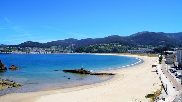 A coastal beach with a clear sky, a sandy shore, and a backdrop of mountains. - Apartamentos Duerming Sea View Viveiro (Viveiro)