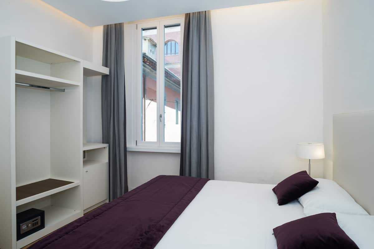 Habitación de hotel con cama, armario y ventana con cortinas.