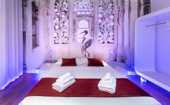 A room with a large bed, two red pillows, a white bath, and a decorative wall with a bird.