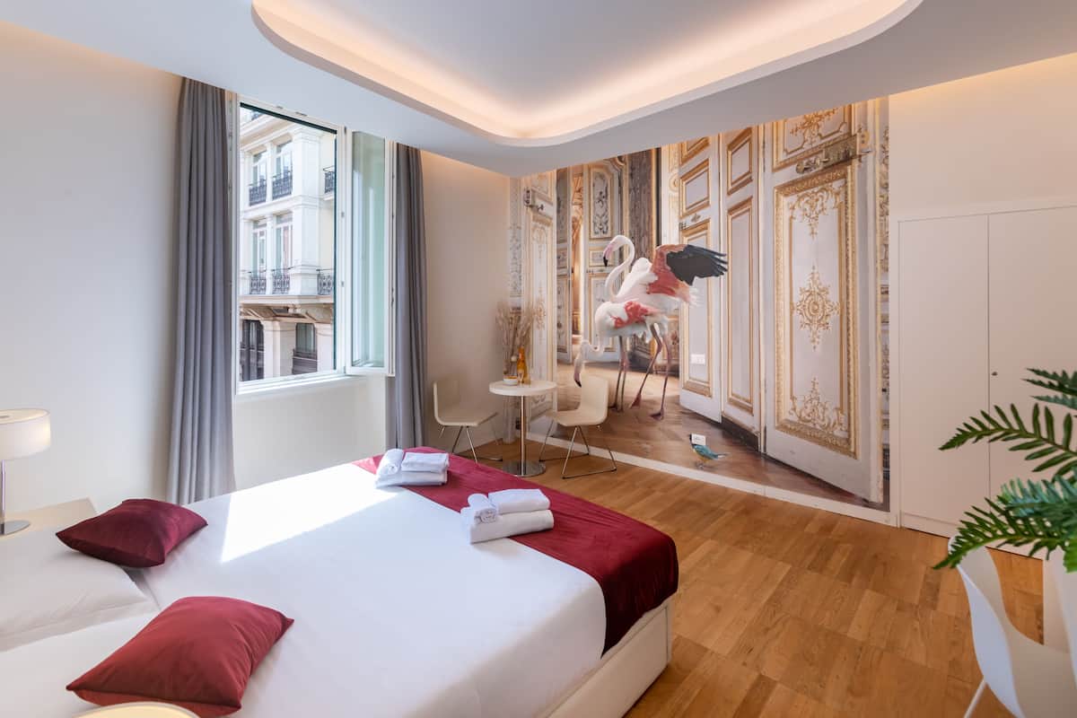 Habitación de hotel con una cama grande, un escritorio, una silla y vistas de la ciudad a través de la ventana.