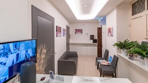 A modern hotel room with a large flat-screen TV, a desk with a chair, a sofa, and a dining area with a table and chairs. - Trevi Elite Rome (Rome)