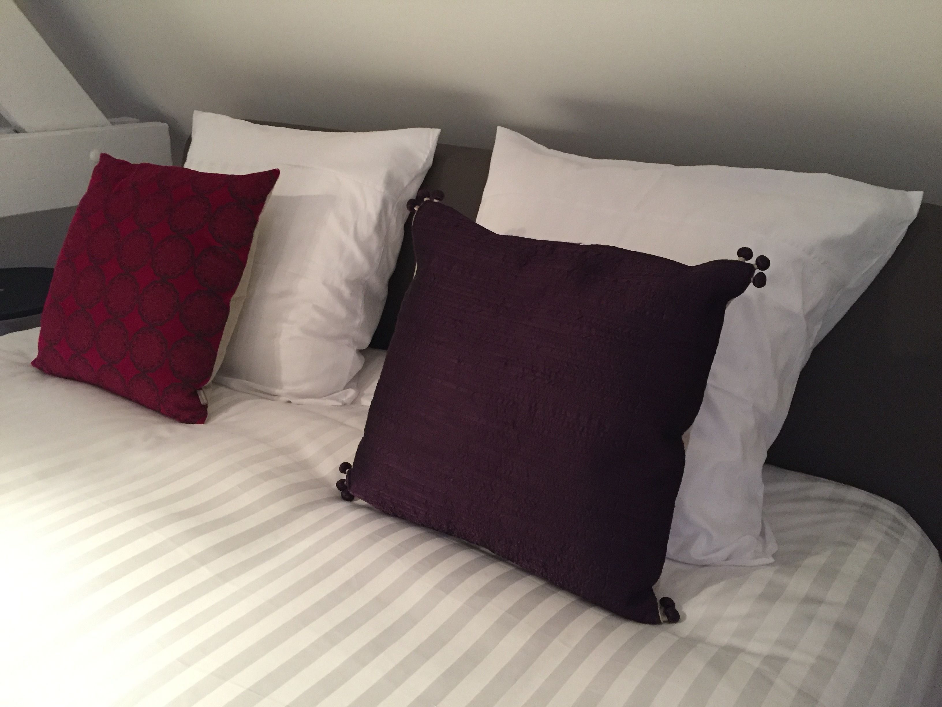 Una cama con ropa de cama a rayas y tres almohadas de distintos colores.