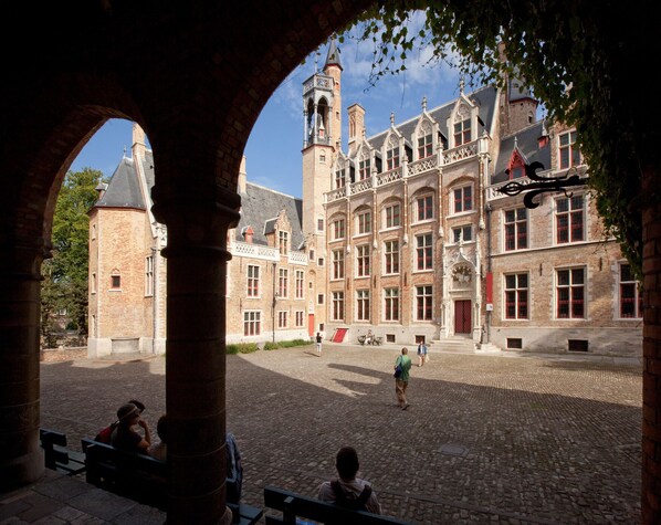 A courtyard with a historic building featuring a tower, a covered walkway, and a cobblestone ground.