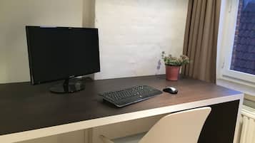 A computer desk with a monitor, keyboard, and mouse. There is a potted plant on the desk.