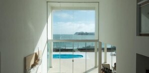 A modern interior with a large glass window overlooking a pool and a beach. - Villa Areia Branca Buzios (Búzios)