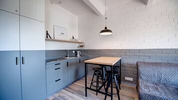 A compact kitchen with grey cabinets, a wooden table, and black stools.