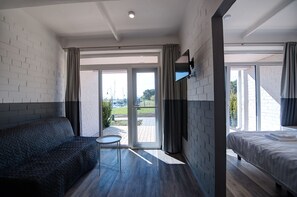 A modern hotel room with a sofa, a small table, a bed, and large windows offering a view of the outdoors. - Smiltynes Jachtklubas (Klaipeda)