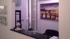 A room with a desk, a chair, a framed picture of a cityscape, and a wall clock listing various cities. - Roman Enchantment (Rome)