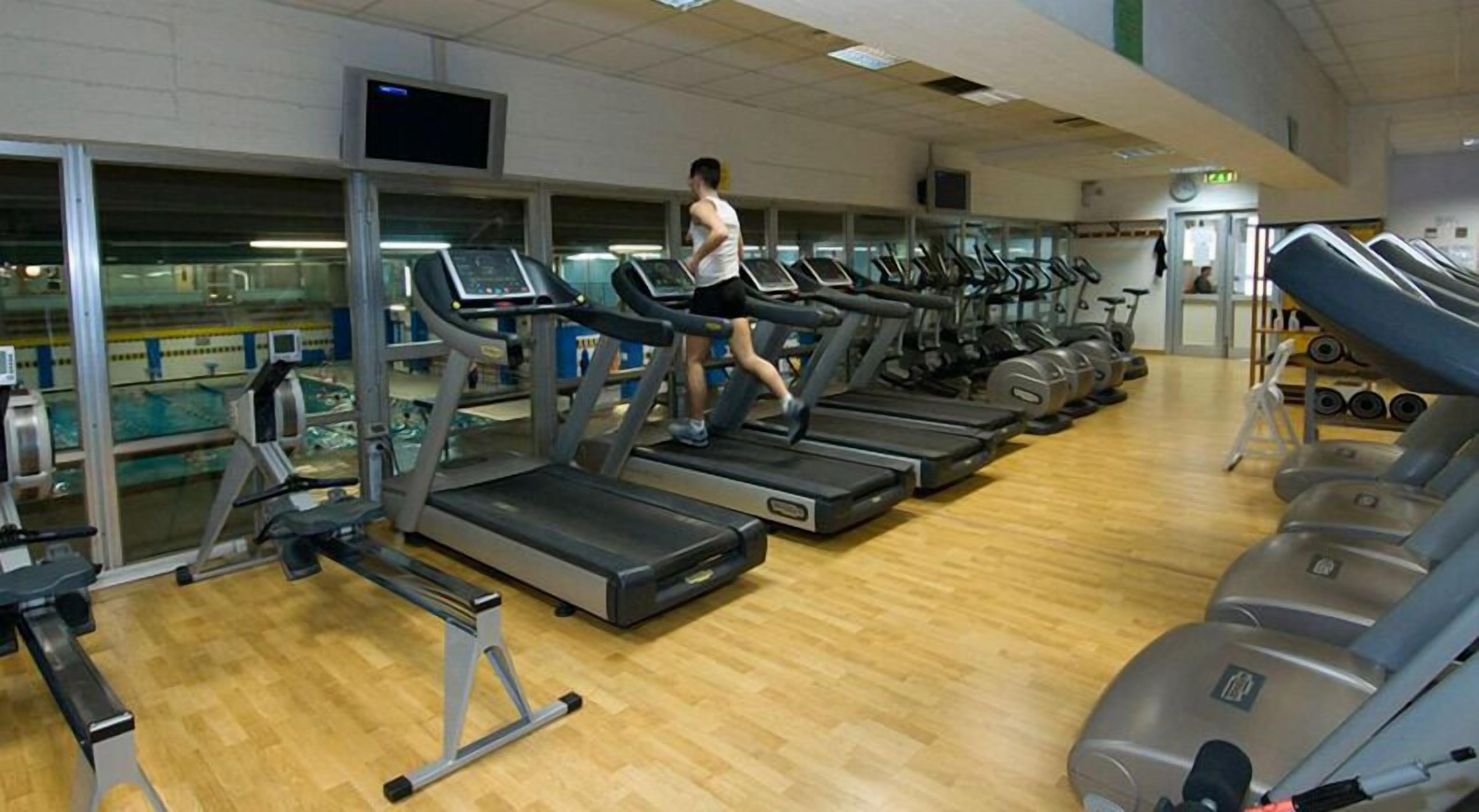 A gym with multiple treadmills, weight machines, and a wooden floor.