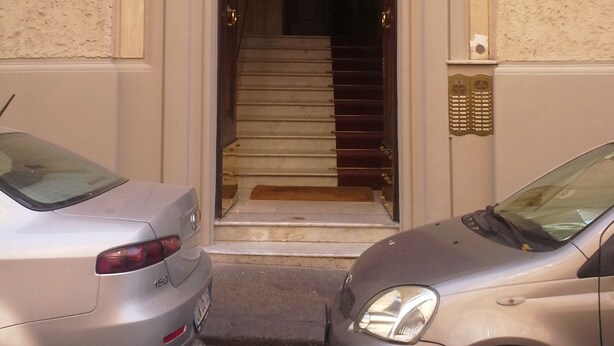 A building entrance with a staircase leading inside, a door with a number plate, and a car parked in front. - Roman Enchantment (Rome)