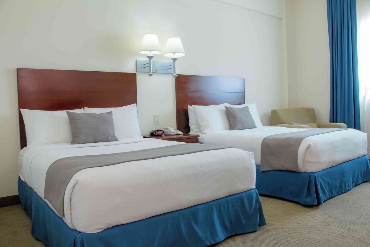 A hotel room with two beds, each with a headboard, bedside tables, lamps, and a telephone.