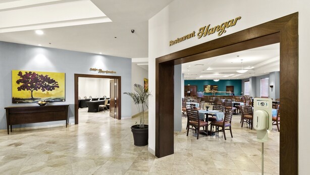 A restaurant interior with a dining area, a reception desk, and a painting on the wall.