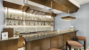 A bar area with a long counter, multiple shelves of bottles, and two stools with patterned cushions.