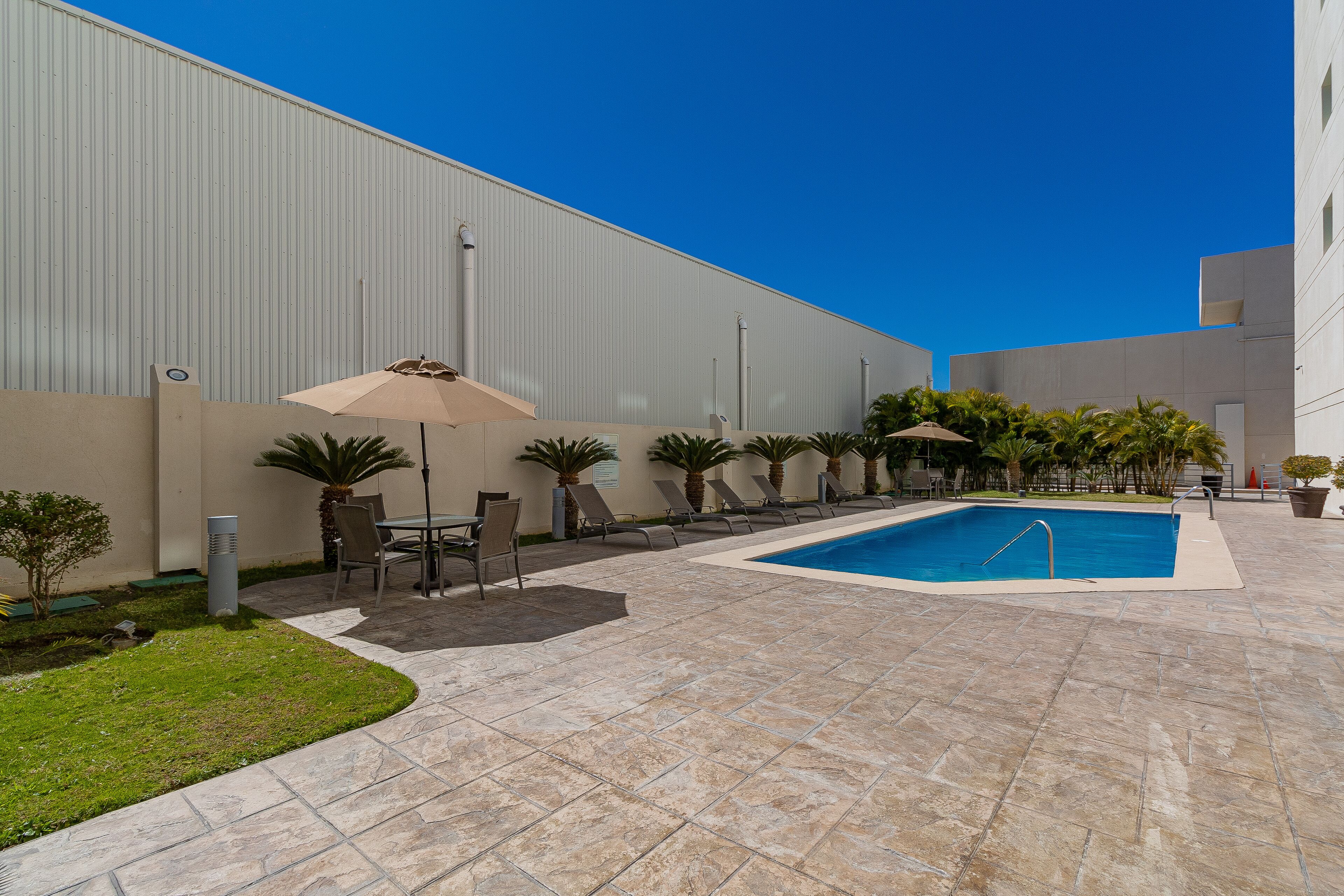 A swimming pool with lounge chairs and umbrellas, surrounded by a tiled patio area.