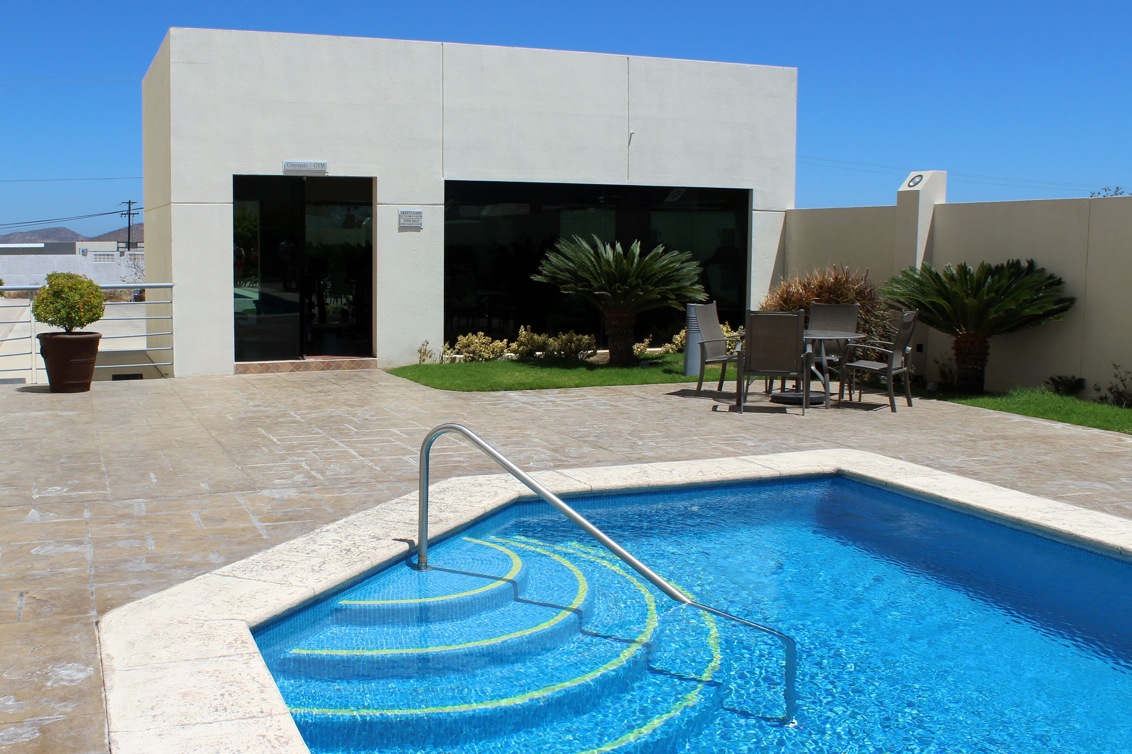 A swimming pool with a metal ladder, surrounded by a patio area with chairs and potted plants.