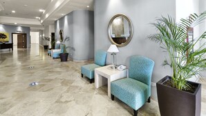 A hotel lobby with seating areas, a reception desk, and a large mirror on the wall.
