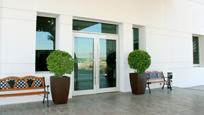 A building entrance with glass doors, two potted plants, and a bench.