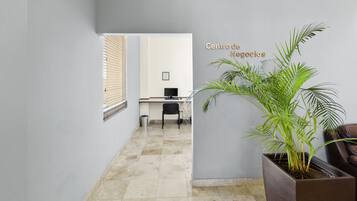 A hallway with a potted plant, a desk with a computer, and a sign reading "Centro de Negocios".