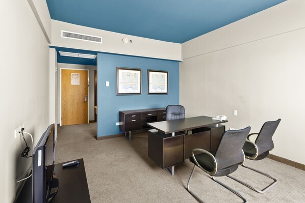 A conference room with a dark brown table, two chairs, a wooden door, and two framed pictures on the wall.